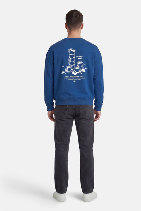 Blauwe sweater met ronde hals van KAOTIKO, met koffiekopjes-print en tekst op de rug.