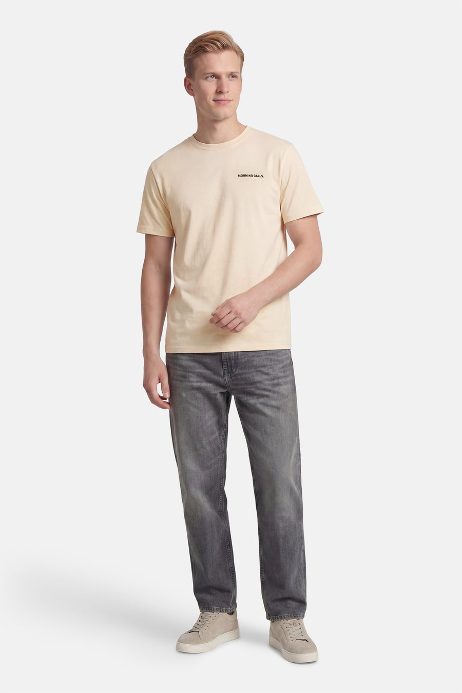Ecru T-shirt van KAOTIKO met korte mouwen, en zwarte tekst "Morning Calls." rechtsboven. Gekleed met een grijze jeans en lichte sneakers.