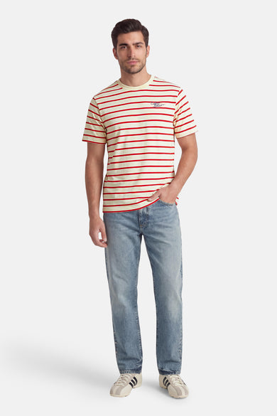 T-shirt multicolore de KAOTIKO, avec des rayures rouges et un imprimé texte bleu foncé, combiné avec un jean bleu et des baskets couleur crème.