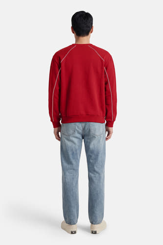 Pull rouge à col rond de KAOTIKO, avec coutures blanches sur les épaules, combiné avec un jean bleu et des baskets crème, vu de dos.