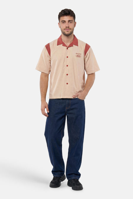 Chemise multicolore à manches courtes de KAOTIKO, beige avec des accents brun-rouge, des boutons rouges et des broderies, portée par un homme en jean et baskets.