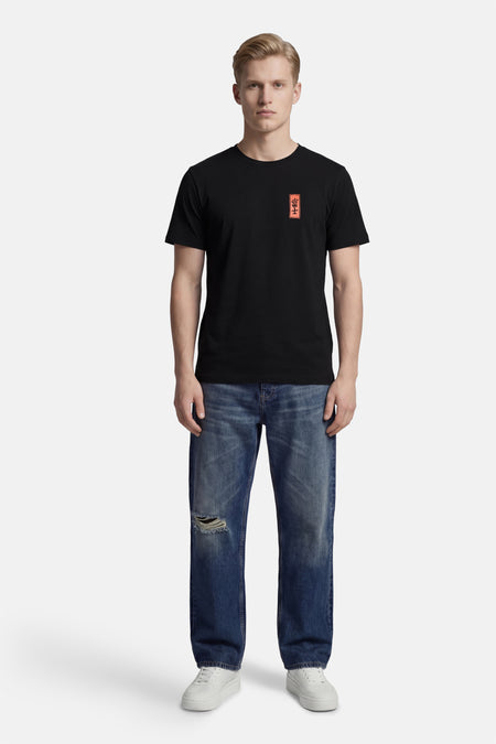 Zwart T-shirt met korte mouwen van KAOTIKO, met een klein rood embleem, gecombineerd met blauwe jeans en witte sneakers.
