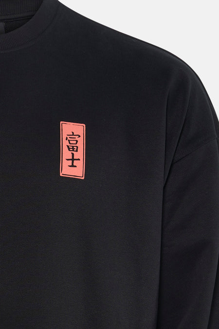 Zwarte sweater van KAOTIKO, met een rechthoekig patch met Japanse karakters op de borst.