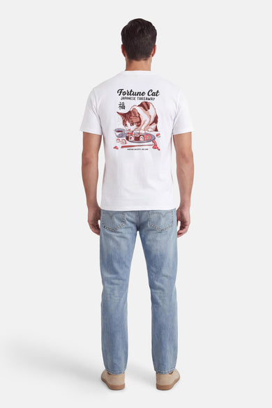 T-shirt blanc de KAOTIKO, avec un imprimé de chat et de sushis au dos, porté avec un jean bleu et des chaussures en daim.