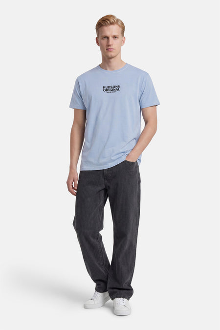 T-shirt bleu de KAOTIKO avec imprimé texte 'HUDSONS ORIGINAL', porté avec un pantalon foncé et des baskets blanches.