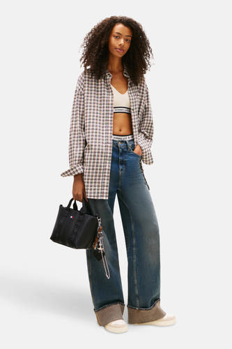 Sac à dos noir de TOMMY JEANS, avec une sangle et des boucles, porté avec un chemisier à carreaux, des jeans larges et des baskets basses.