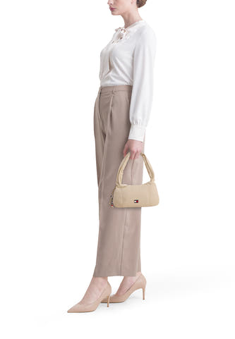 Beige schoudertas van TOMMY JEANS, met zilverkleurige details en gecombineerd met een witte blouse en beige pantalon met hakken.