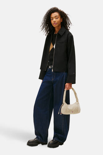 Beige schoudertas van TOMMY JEANS, met ritssluiting en gedetailleerde stiksels, gedragen met een zwarte jas en wijde jeans.