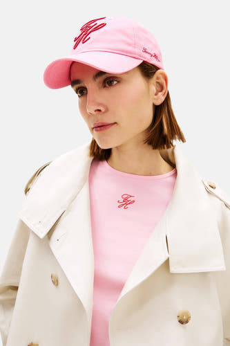 Roze pet van TOMMY JEANS, met geborduurd logo en gedragen met een roze shirt onder een beige trenchcoat.
