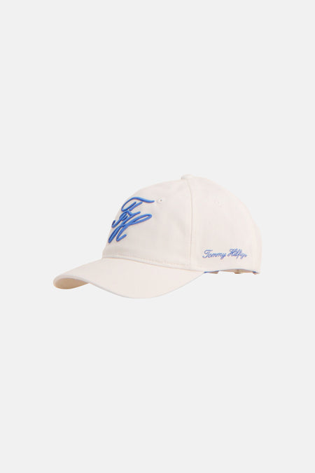 Witte pet van TOMMY JEANS met blauw geborduurd logo op de voorkant en Tommy Hilfiger handtekening opzij, in zijaanzicht.