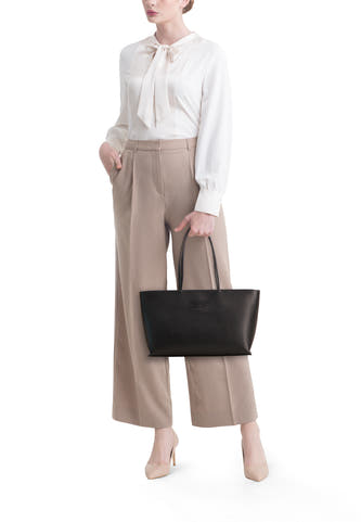 Sac à bandoulière noir TOMMY JEANS avec logo gaufré, porté par un mannequin en chemisier blanc et pantalon beige.