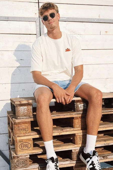 Ecru T-shirt met korte mouwen van BASELAB, gedragen met denim shorts en sneakers, zittend op houten pallets.
