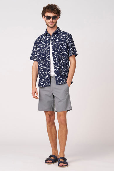 Blauwe bermuda van Bruce & Butler, gecombineerd met een wit hemd en een open donkerblauw overhemd met print.