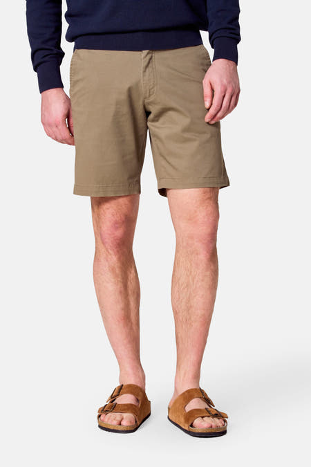 Kaki bermuda van Bruce & Butler, gedragen met een donkerblauwe trui en bruine sandalen.
