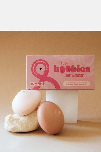 Roze verzorgingsproduct van WONDR CARE, gepresenteerd met zeepjes in de vorm van borsten op een beige achtergrond.

