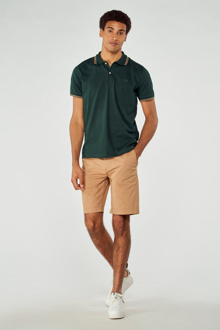 Bruine bermuda short van Bruce & Butler, gedragen met een donkergroene polo en witte sneakers.
