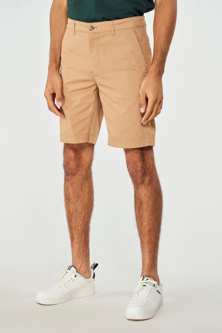 Bruine short van Bruce & Butler, met een effen dessin, gedragen met een groen shirt en witte sneakers.
