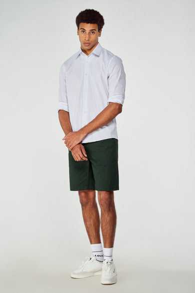 Short bermuda vert de Bruce & Butler, porté avec une chemise blanche et des baskets blanches, vue de face.