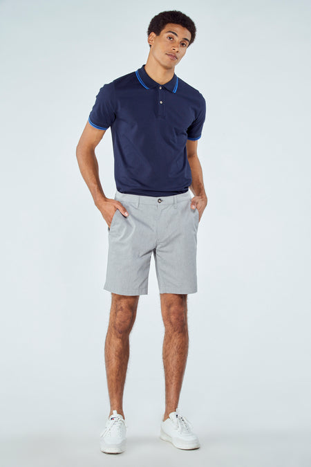 Blauwe short van Bruce & Butler, gecombineerd met een marineblauwe polo met blauwe accenten en witte sneakers.