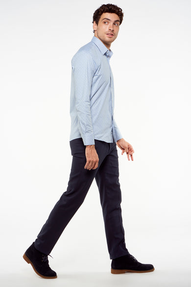 Blauwe kostuumbroek van Bruce & Butler, gedragen met een lichtblauw overhemd en suède schoenen, in zijwaarts lopende positie.
