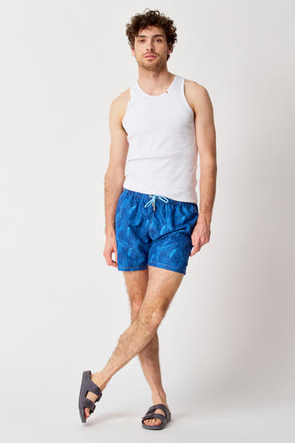 Blauwe zwemshort van Bruce & Butler, met bladerpatroon, gecombineerd met wit hemd en sandalen.
