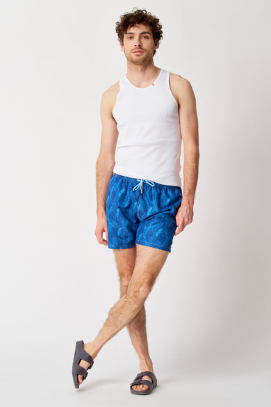 Blauwe zwemshort van Bruce & Butler, met bladerpatroon, gecombineerd met wit hemd en sandalen.
