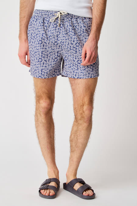 Blauwe zwemshort van Bruce & Butler met bloemenprint, gedragen met sandalen en een wit hemd.
