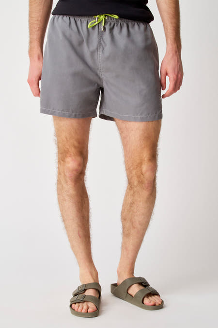 Grijze zwembroek van Bruce & Butler, met groene koordjes en gedragen met olijfgroene sandalen.