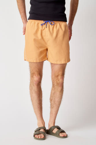 Pantalon de bain Bruce & Butler, avec une ceinture bleue et porté avec des sandales vertes.