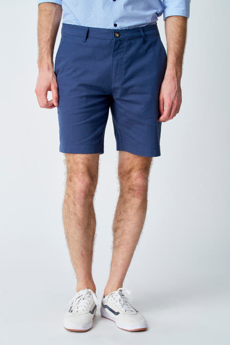 Blauwe short van Bruce & Butler, met witte sneakers gedragen tegen een effen achtergrond.
