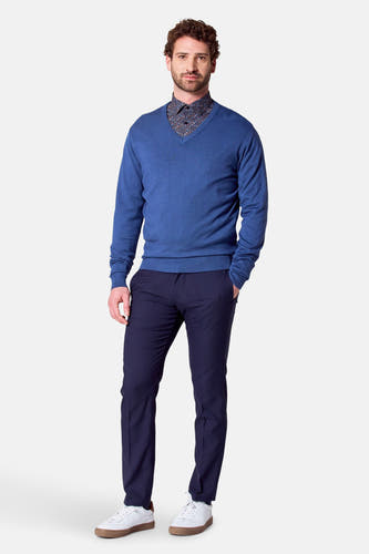 Blauwe V-hals trui van Bruce & Butler, gecombineerd met een overhemd met print en donkerblauwe broek.