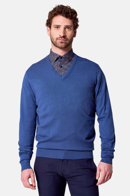Blauwe V-hals trui van Bruce & Butler, gedragen over een overhemd met print, met lange mouwen en donkere pantalon.