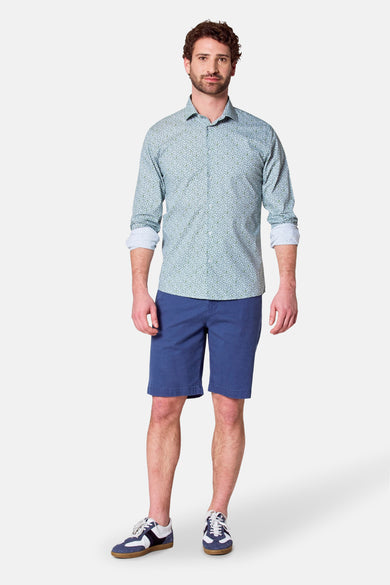 Man met overhemd met print en blauwe shorts, staand.