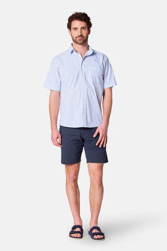Lichtblauw overhemd met korte mouwen van Bruce & Butler, met een fijn patroon, gecombineerd met donkerblauwe shorts en sandalen.
