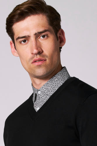 Pull noir à col V de Bruce & Butler, porté sur une chemise à imprimé floral.