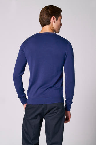 Blauwe V-hals trui van Bruce & Butler, achterkant zichtbaar, gecombineerd met donkere pantalon.
