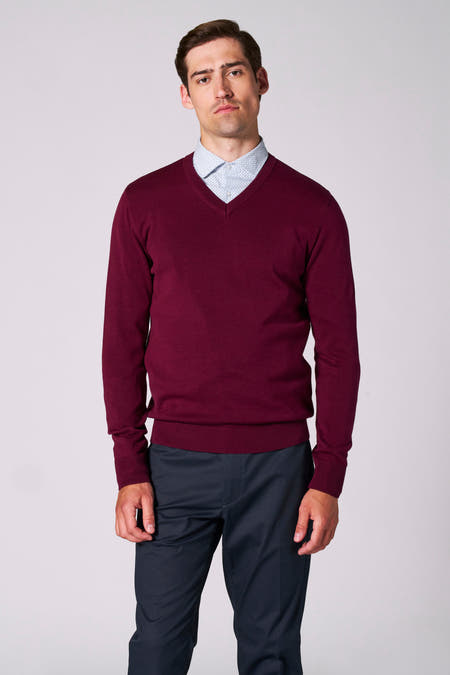Bordeaux trui met V-hals van Bruce & Butler, gedragen over een lichtblauw overhemd met print en donkere pantalon.
