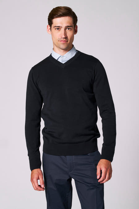 Donkerblauwe V-hals trui van Bruce & Butler, gedragen over een lichtblauw overhemd met print en een donkere pantalon.
