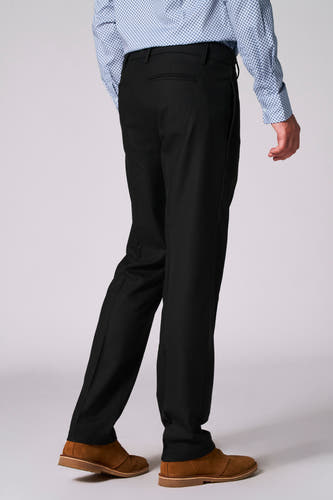 Zwarte kostuumbroek van Bruce & Butler, met achterzak, gecombineerd met een overhemd met blauw patroon en suède schoenen.
