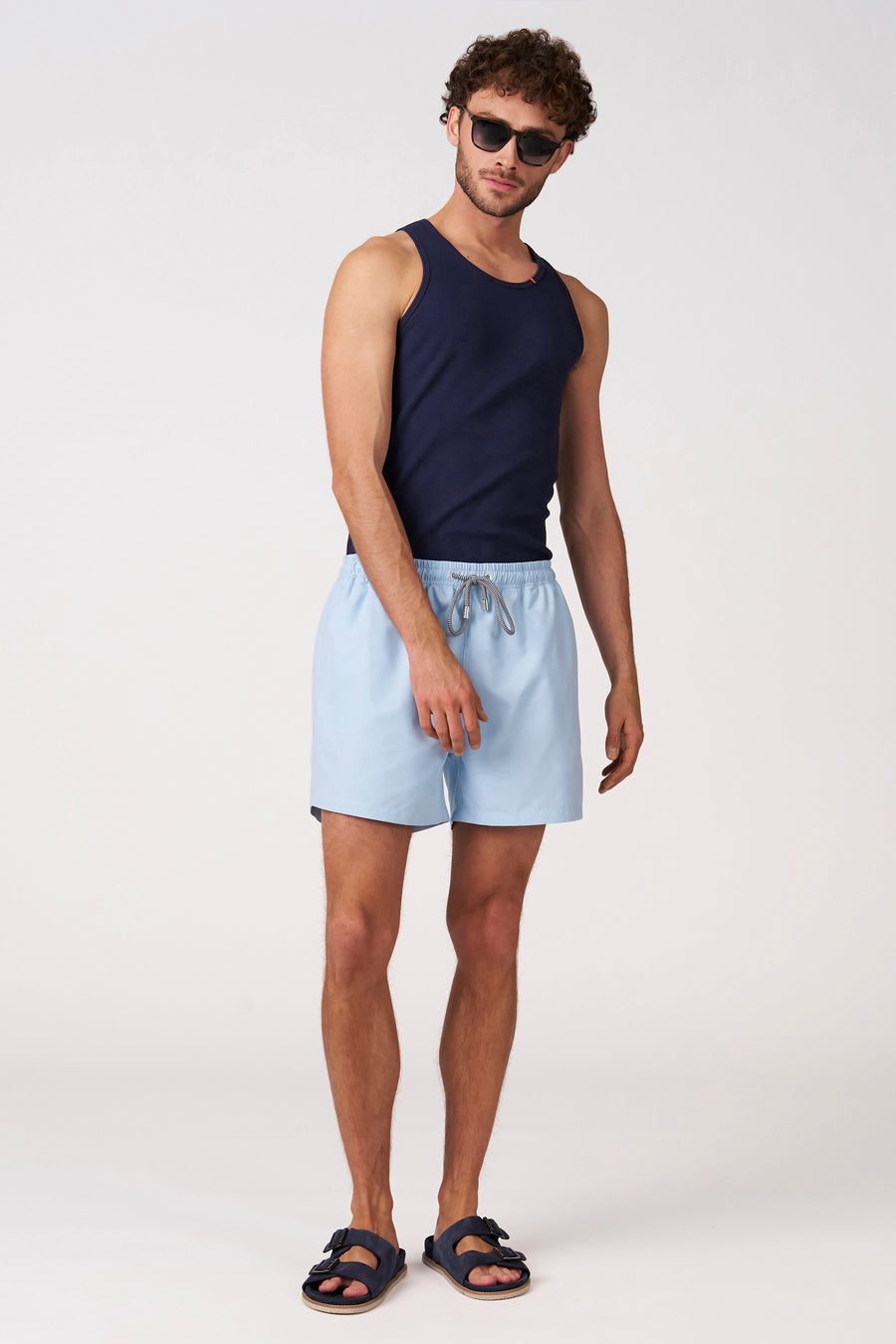 Short de bain bleu de Bruce & Butler avec cordons de serrage rayés, porté avec un débardeur côtelé bleu foncé et des sandales.