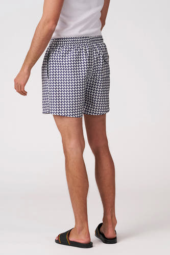 Blauw-witte pied-de-poule zwemshort van Bruce & Butler, gedragen door een man van achteren met een witte tanktop en zwarte sandalen.