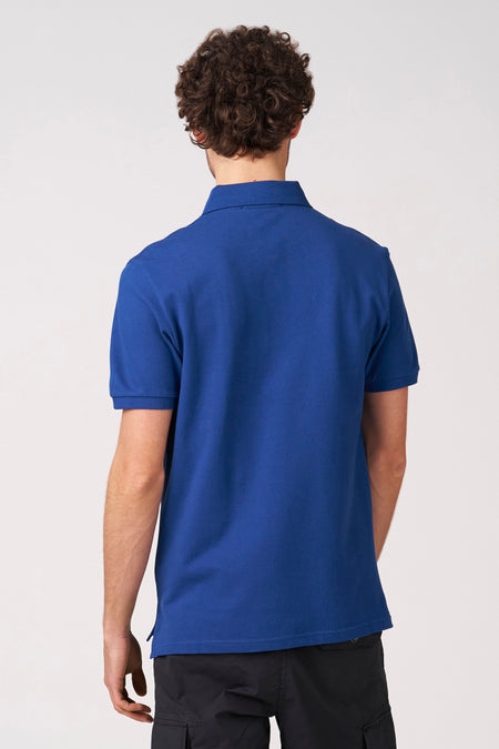 Blauw poloshirt met korte mouwen van Bruce & Butler, gezien van achteren, gedragen met een zwarte broek.