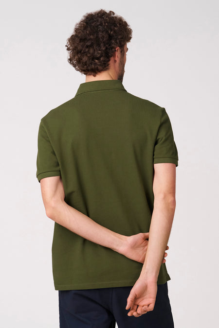 Groene polo met korte mouwen van Bruce & Butler, achterkant te zien met gekruiste armen en donkere broek.
