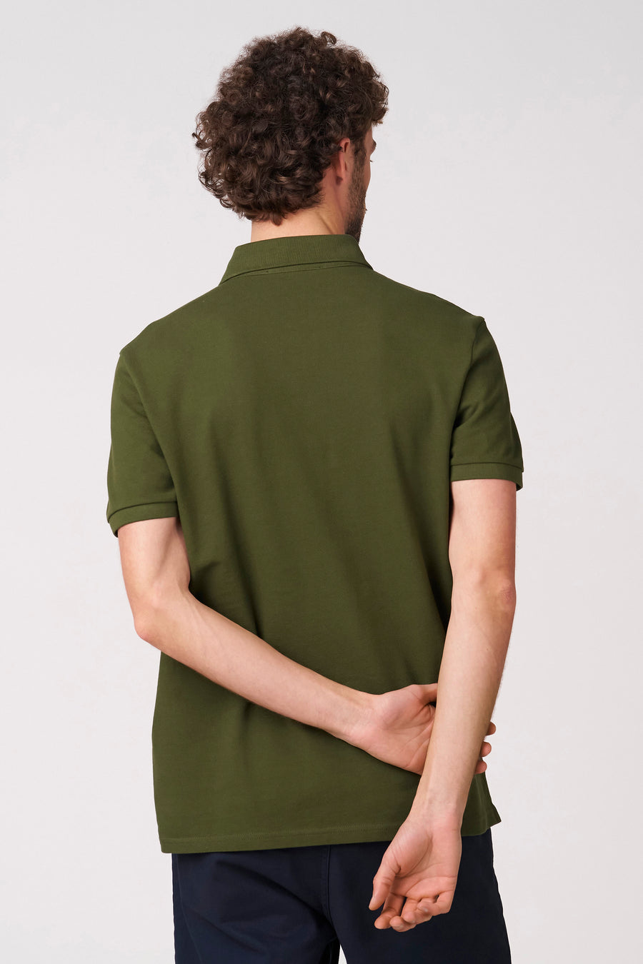 Groene polo met korte mouwen van Bruce & Butler, achterkant te zien met gekruiste armen en donkere broek.
