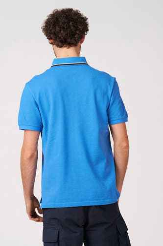 Blauwe polo met korte mouwen van Bruce & Butler, gezien van achteren met een gestreepte kraag en donkere cargo broek.
