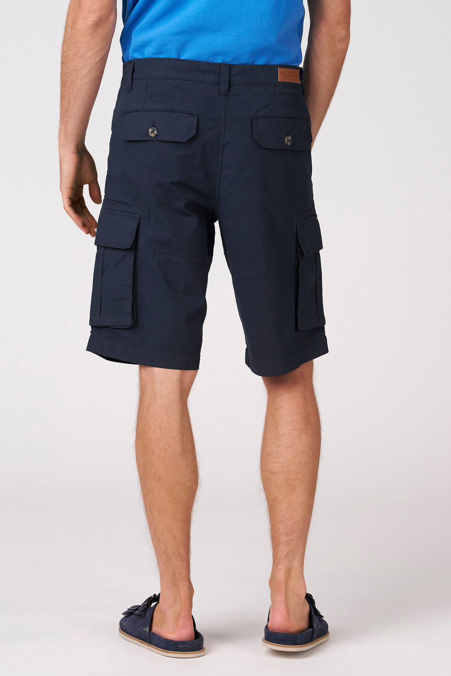 Blauwe Bermuda shorts van Bruce & Butler, achterkant met zakken, model in blauw shirt en slippers