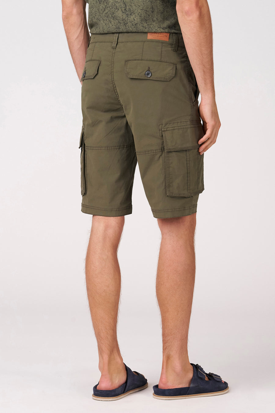 Kaki Bermuda's van Bruce & Butler, achterkant met zakken, casual stijl, model draagt donkergroen shirt en blauwe slippers