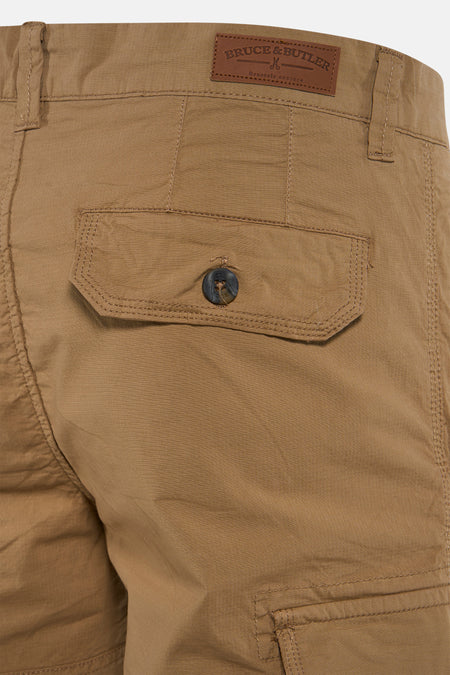 Beige Bermuda shorts van Bruce & Butler, achterzijde met bruin leerlabel en donkere knoop op zak, textuurrijke stof, close-up.