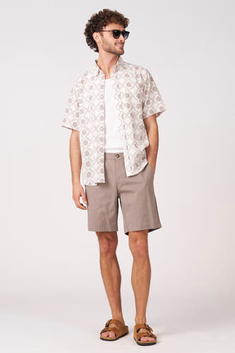 Chemise à manches courtes colorée de Bruce & Butler, avec un motif floral graphique, combinée à un t-shirt blanc et un short marron.