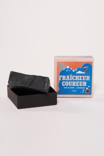 Savon noir de Cyclo Club Marcel, dans une boîte noire à côté d'un emballage avec étiquette.